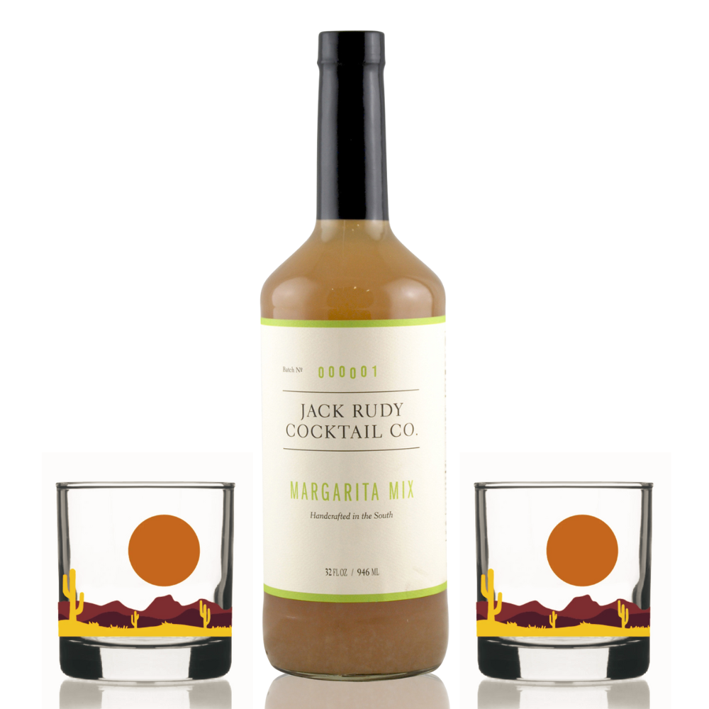 Bottle of Jack Rudy Cocktail Co. margarita mix with two glasses featuring a desert design on a white background.